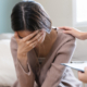 Front view of young woman crying while a doctor puts supportive hand on her shoulder, in clinical setting