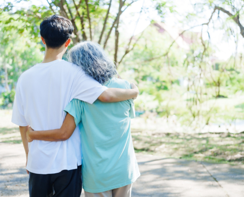 A happy senior mother embraces her smiling adult son in a lush green park